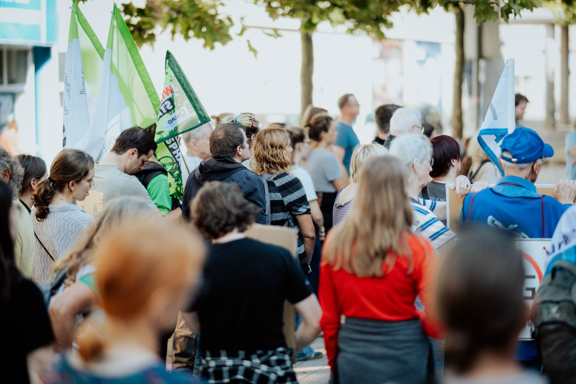 Auf dem Bild stehen protestierende Menschen auf der Rambla in Wilhelmshaven. Einige von ihnen halten Fahnen und Schilder.